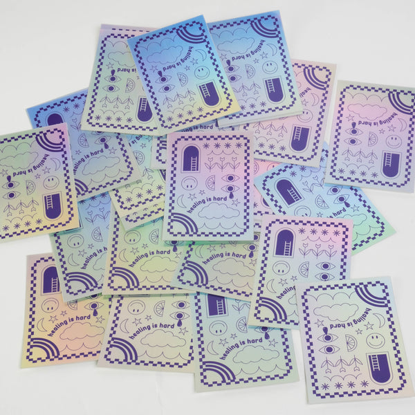 A flat white background with a collage of "healing is hard" holographic stickers.