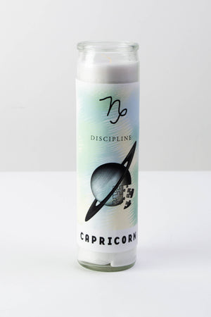 A tall glass votive candle with symbols representing the astrological sign of Capricorn.