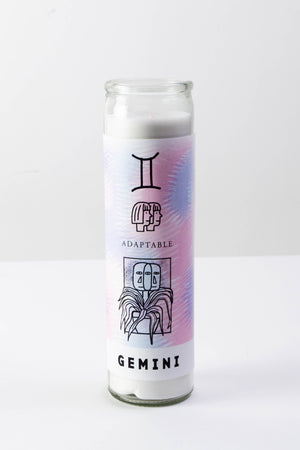 A tall glass votive candle with a purple and pink decal depicting illustrations for the astrological sign "Gemini."