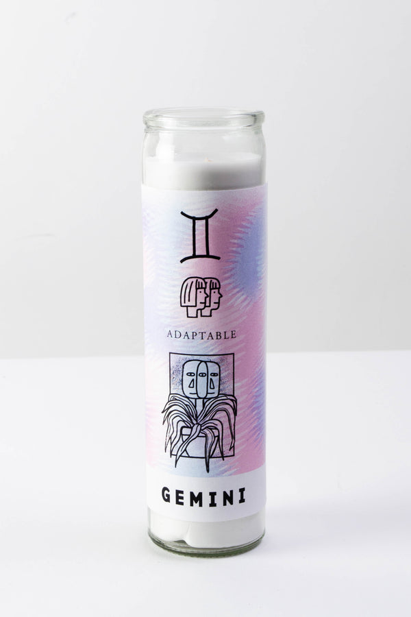 A tall glass votive candle with a purple and pink decal depicting illustrations for the astrological sign "Gemini."