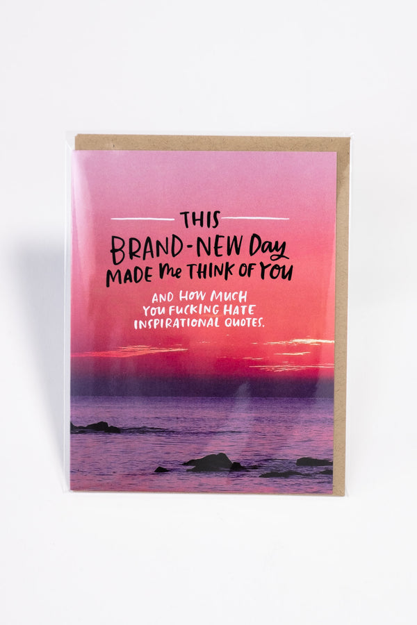 A greeting card showing the ocean with a pink and purple sunset. The card reads "this brand-new day made me think of you and how much you fucking hate inspirational quotes."