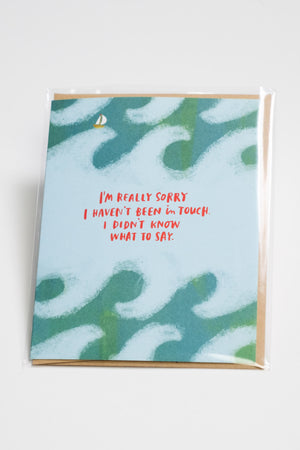 A greeting card with a watercolor-esque depiction of waves and a small sailboat. The red text reads "I'm really sorry I haven't been in touch. I didn't know what to say."