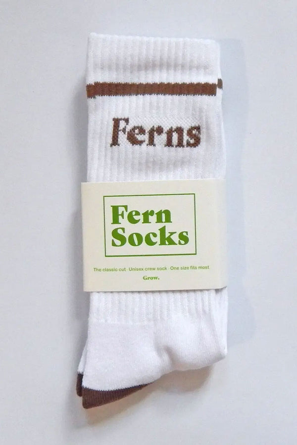 Folded pair of white crew socks on a white background. The top of the socks feature a brown strip and the word Ferns in brow lettering. A Paper sleeve is wrapped around the socks. in green lettering the sleeve says Fern Socks. The Classic cut. Unisex crew sock. One size fits most.