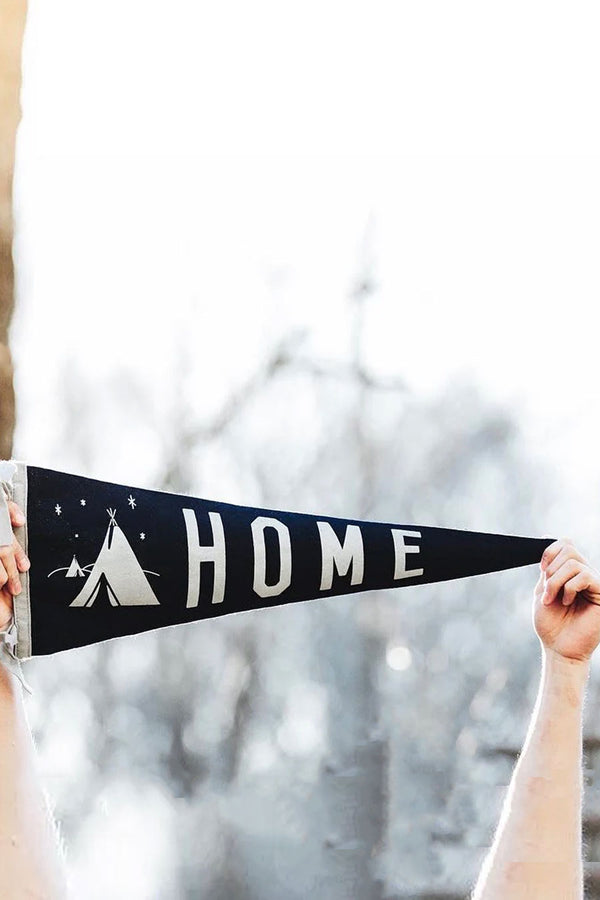 A Person holding a  navy pennant with a white edge. Next to an illustration of a tent under the stars are the words "Home" in white letters. 
