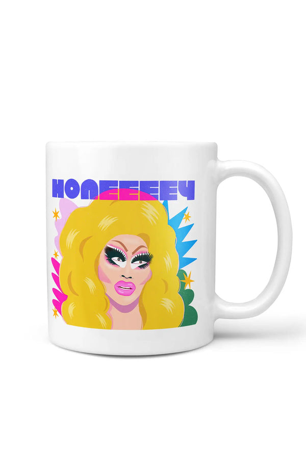 White mug against a white backdrop. The mug features a Drag Queen called Trixie Mattel. Behind her is colorful shapes in pinks and blues, with the word "HONEEEEY" above the image.