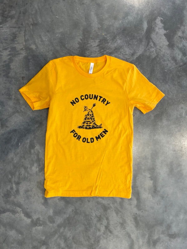 Yellow tshirt on gray concrete background. The design on the shirt has black text circling a snake that has an arrow through it and it reads No country for Old men.
