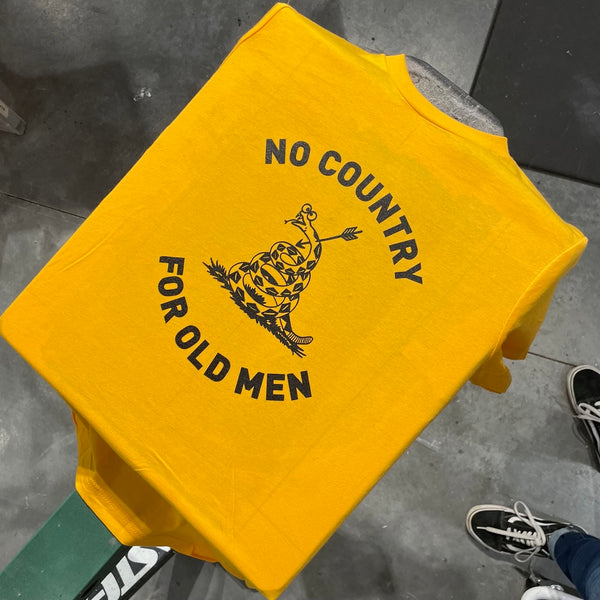 Yellow Tshirt on a screen printing press. The design is black with a text that reads No country for old men surrounding an illustrated snake that has an arrow through it.