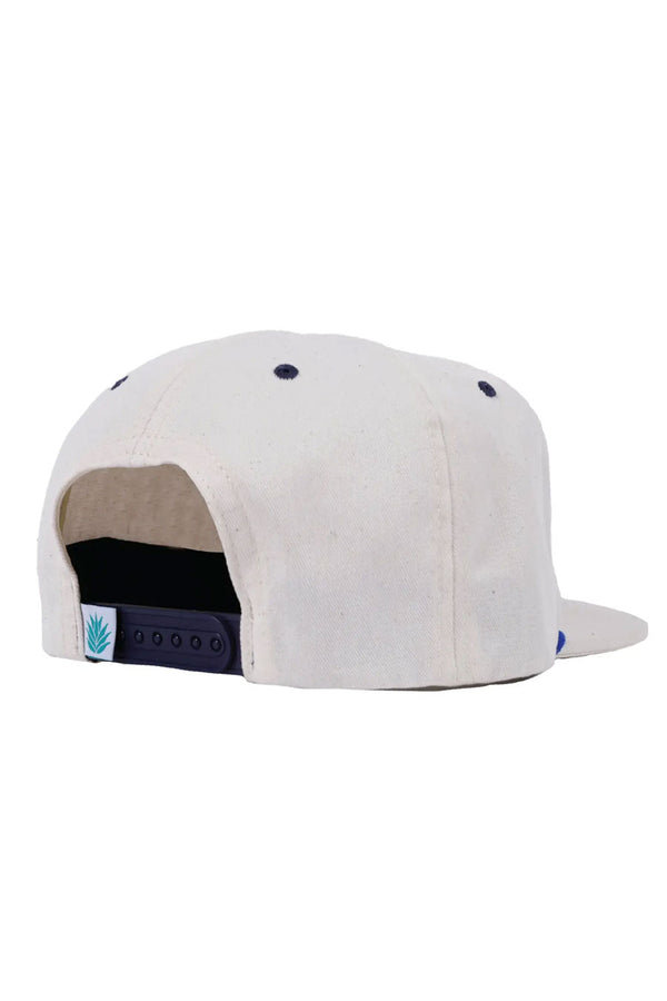 Backview of white canvas hat with a plastic navy clasp. The tag next to the snaps is a white cloth tag with a green agave plant. 
