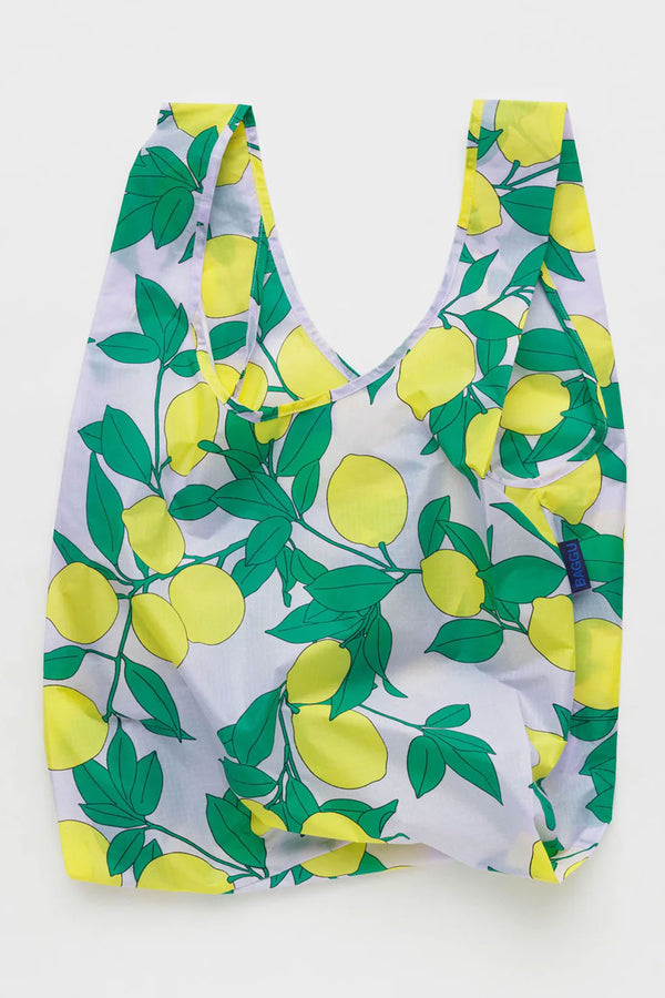 White reusable tote bag featuring yellow lemons and green leaves all over it. White background.