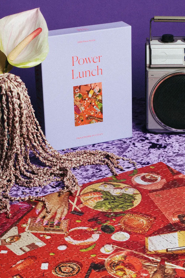 A photograph of a completed Power Lunch puzzle sitting on a purple tablecloth next to a boombox and a calla lily.
