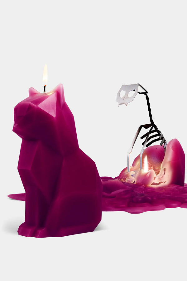 Dark pink geometric shaped cat candle. Behind that candle is a melted cat candles that exposed a metal skeletal frame of a cat. White background.