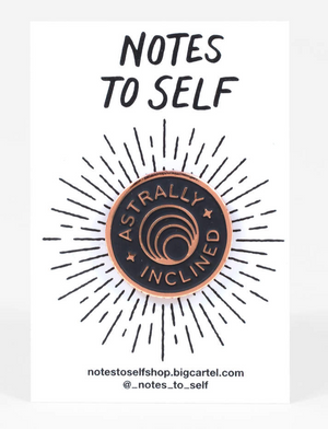 An enamel pin showing concentric circles with text that reads "Astrally Inclined."