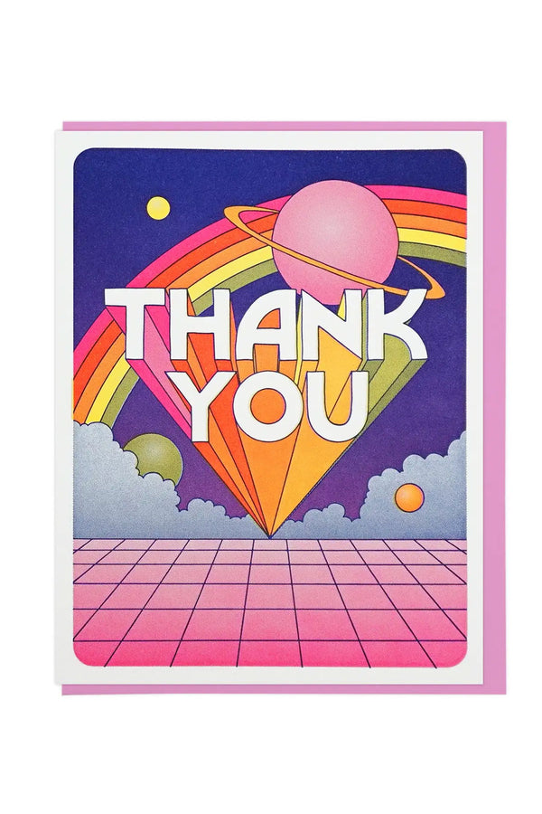 White card with pink envelope on a white background. The card features a blue sky with a rainbow and a pink planet with a yellow ring. Below the rainbow in white text the card says Thank You in block letters that come to a point in rainbow shading. Below the text are blue clouds that sit on top of a pink tile floor.