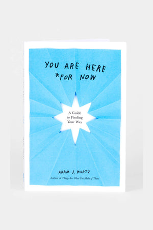 A book is sitting on a white surface. The cover is light blue with a white rectangular border. The black text reads "You are here *for now, A guide to finding your way. By Adam J. Kurtz, author of Things Are What You Make Of Them."