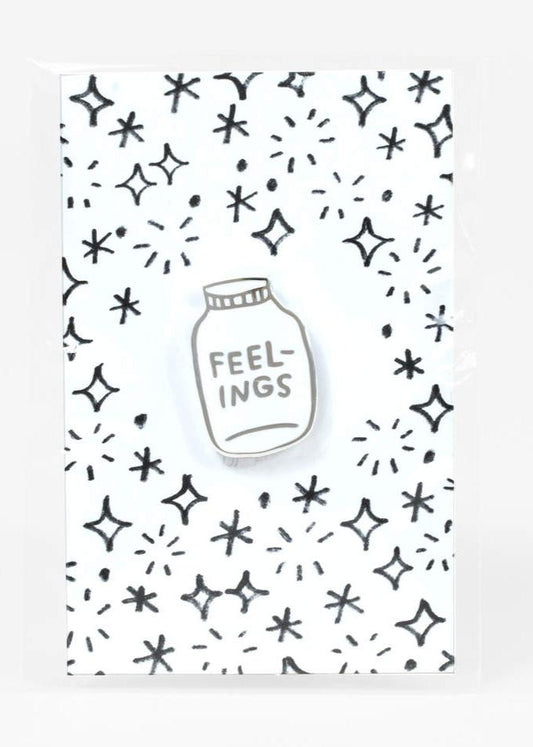 A die-cut enamel pin of a white jar labeled "feelings."