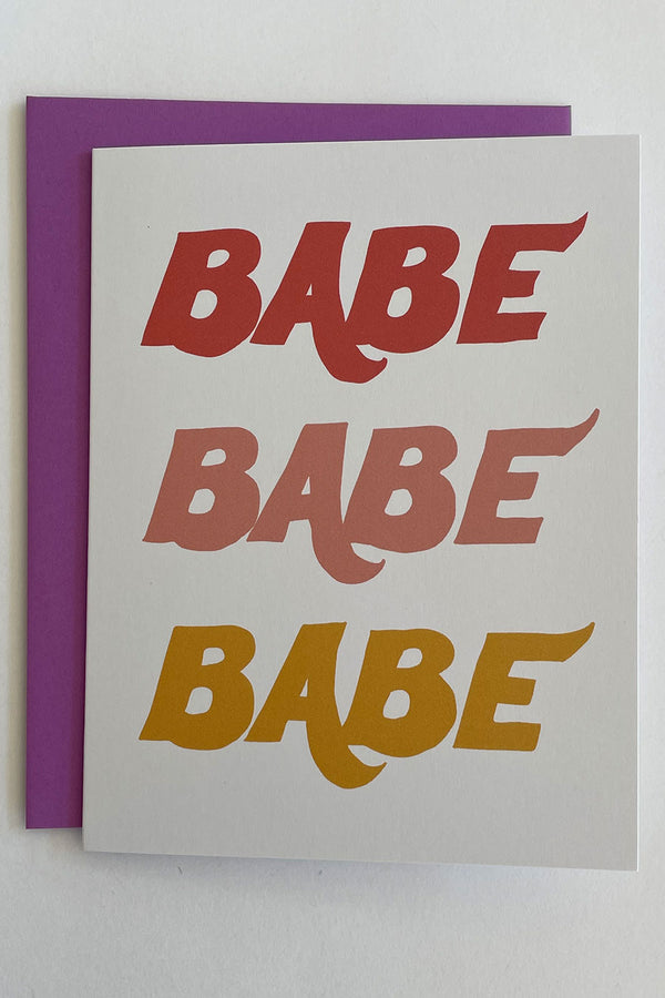 A white greeting card with the words "Babe Babe Babe" written on the front in red, pale pink, and gold letters. Accompanying envelope is purple. 