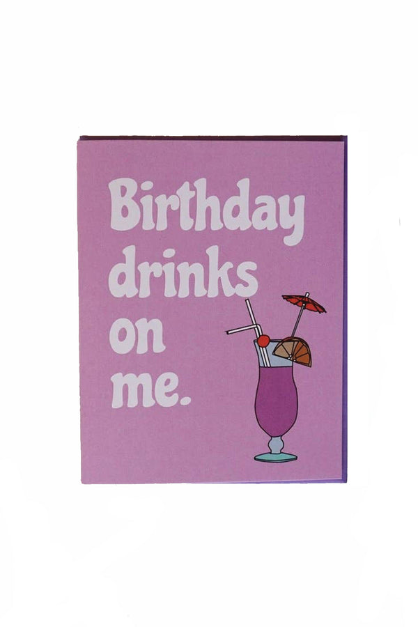 A light purple greeting card depicting a cocktail with a fruit garnish and a drink umbrella. The text reads "birthday drinks on me."
