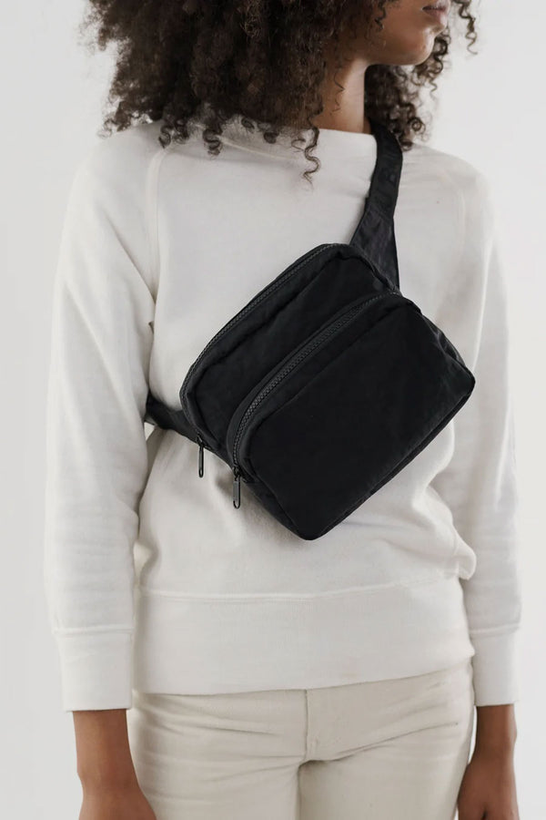 Person wearing black fanny pack with black strap across the body in front of a white background.