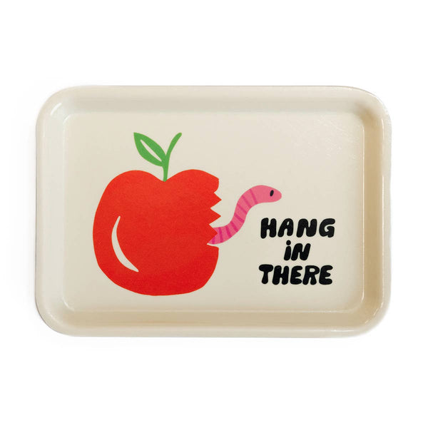White trinket tray on a white background featuring an illustration of a red apple with a green leaf with a bite taken out of it. There is a pink worm sticking out of the apple where the bite was taken out. Next to the apple in black bubble text it says hang in there.