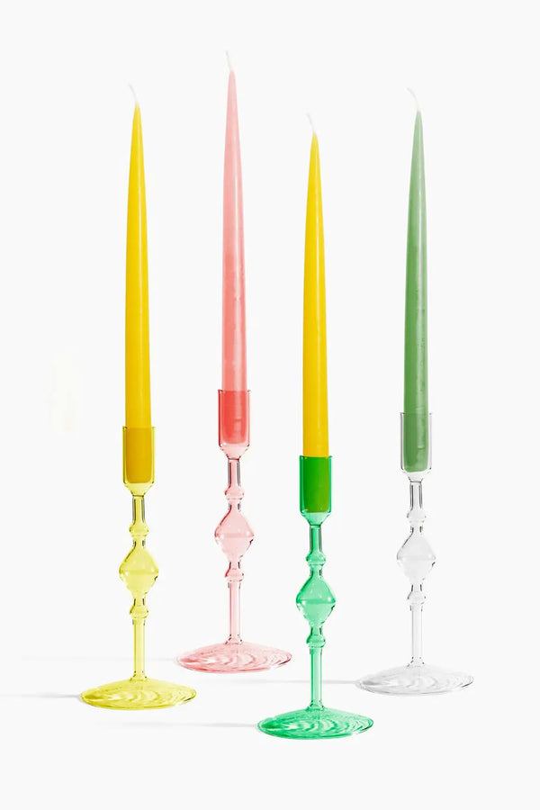 Yellow, pink, green, and clear glass votive candle holders. Each candle holder is holding a tall tapered candle. White background.
