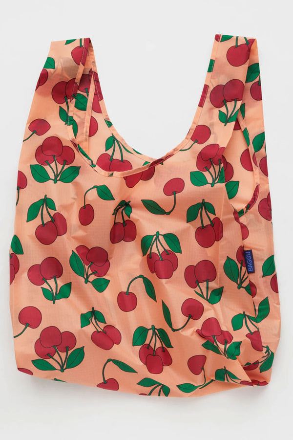 Pink reusable tote bag with cherries and stems printed all over it. White background.