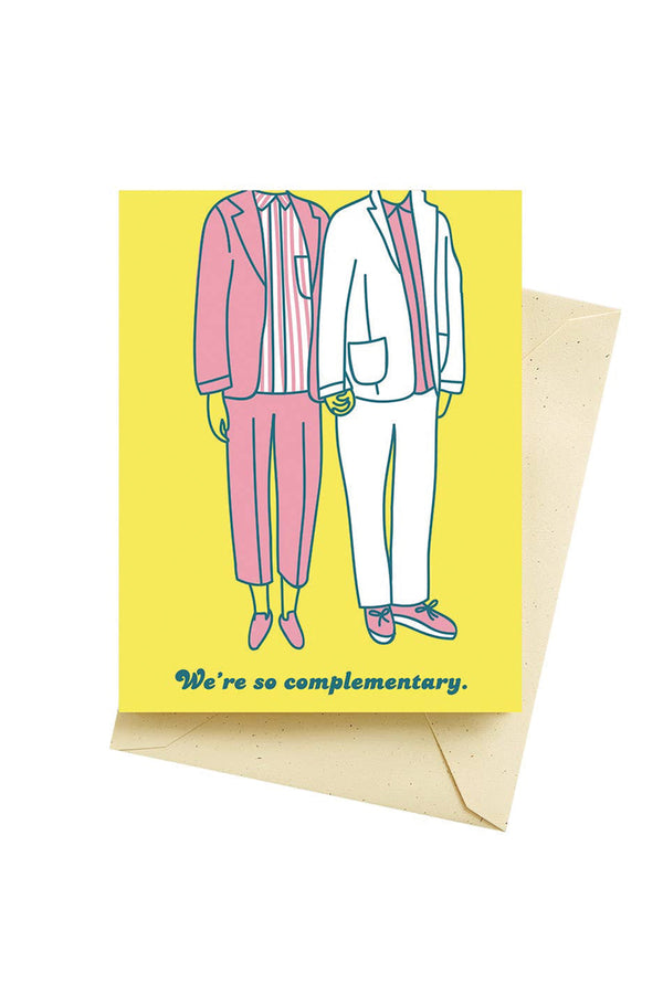 A yellow greeting card with two human figures wearing suits that are pink and white. The text on the card reads "we're complimentary."