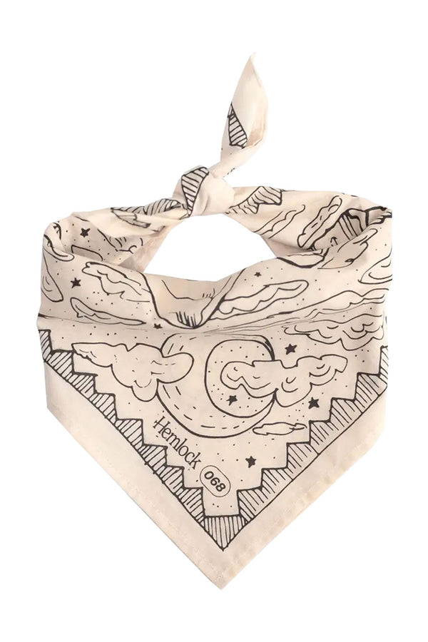 A tan bandana tied into a triangle bib with a pattern of a desert landscape and foliage outlined in black. The background is white.