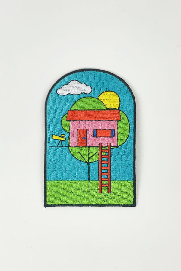 A white background with a colorful embroidered patch depicting a tree house with a telescope next to the front door. The sky is blue and the sun is out.