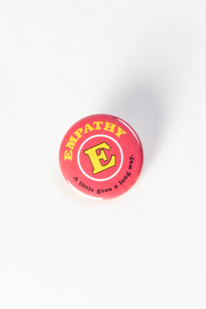 A pink pinback button with yellow and black text that reads "Empathy, a little goes a long way."