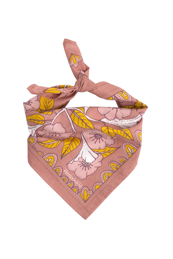 A folded and knotted pale pink bandana on a white background. The bandana has a pattern of gold, white, and pink flowers and foliage.