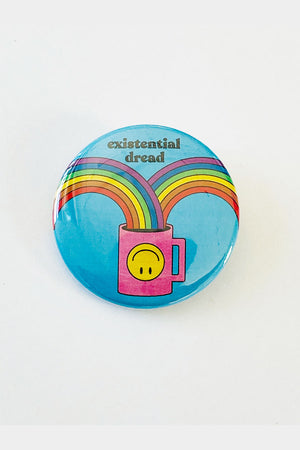 A light blue pinback button with the words "existential dread" and an illustration of 2 rainbows going into a pink coffee cup with a smiley face.