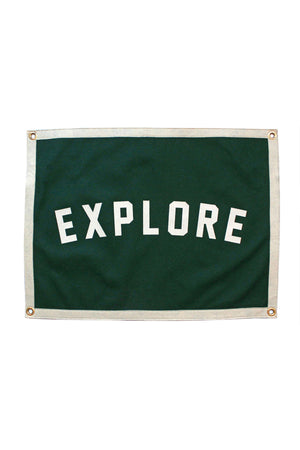 A rectangular forest green felt flag with a white border is on a white background. The flag has 4 gold grommets, one in each corner. The flag says "Explore" in white block letters across the middle. 
