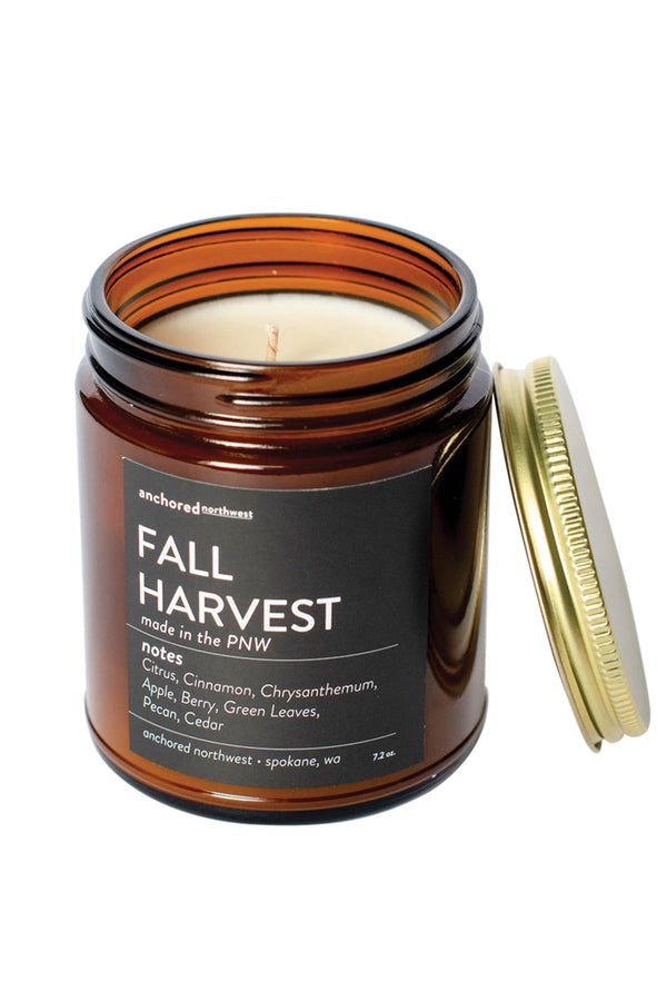 A brown glass jar candle with a gold lid. The candle has a black label, the scent is Fall Harvest.