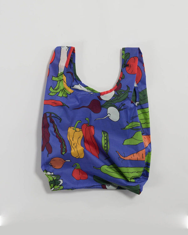 A blue reusable shopping tote with illustrations of vegetables in a variety of colors is on a white background. 