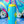 Load image into Gallery viewer, Side view of tall bright blue koozie with yellow retro flowers printed all over it with a bright green frog in the middle. Rainbow swirls with disco balls in the background.

