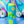 Load image into Gallery viewer, Bright blue tall koozie with yellow retro flowers printed all over it with a bright green frog in the middle. Rainbow swirls with disco balls in the background.
