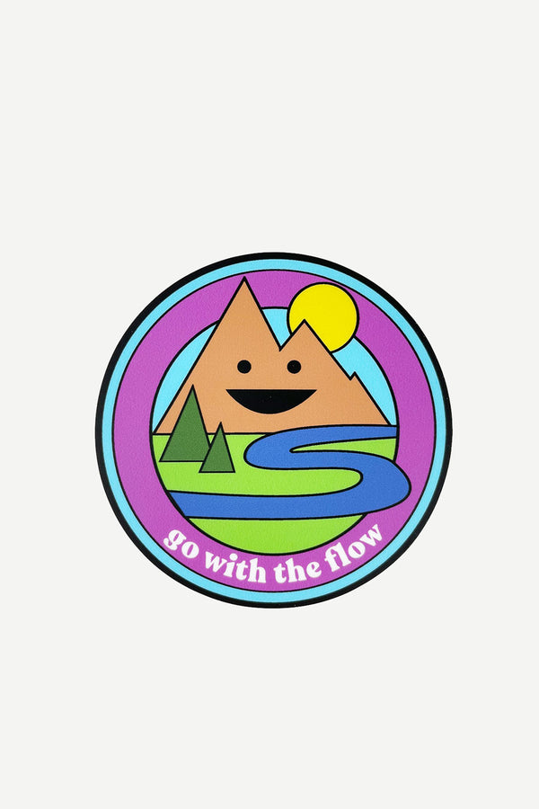 A round sticker with illustrations of a smiling mountain, a flowing river, and some pine trees. The text reads "Go with the flow."