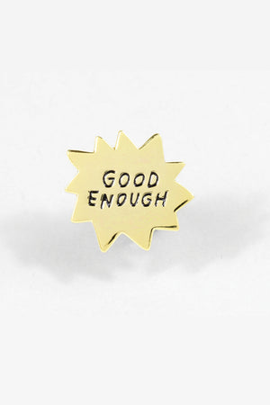Starbust shaped enamel pin in gold. The Pin says Good Enough in black text. White background.