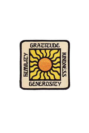 A tan square embroidered patch outlined in black. In the middle is a shining sun. The text reads "gratitude," "kindness," "generosity," and "humility."