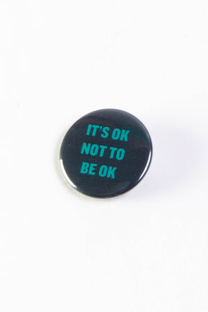 A black pinback button with text that reads "It's ok not to be ok" in teal.