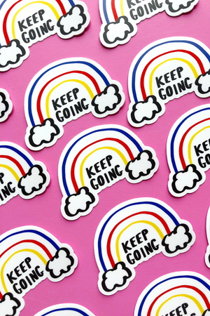  An arrangement of multiple "Keep Going" stickers on a pink background.