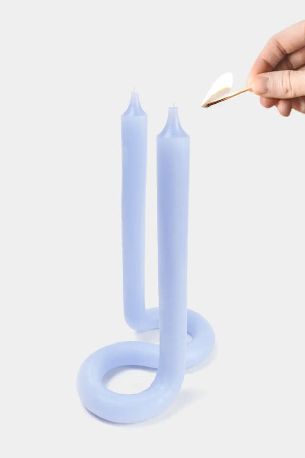Someone with a matchstick lighting a lavender twisted candle with wicks at both ends. White background.