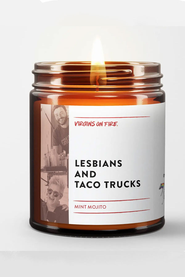 Amber glass candle jar with a white label. The label says Lesbians and Taco Trucks and features a server and customer standing in front of a food truck. Scent is Mint Mojito. White background.