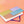 Load image into Gallery viewer, A hard journal with colorblocks of lavender, teal, yellow, and orange features vertical navy stripes laying on its side on a peach glitter background.
