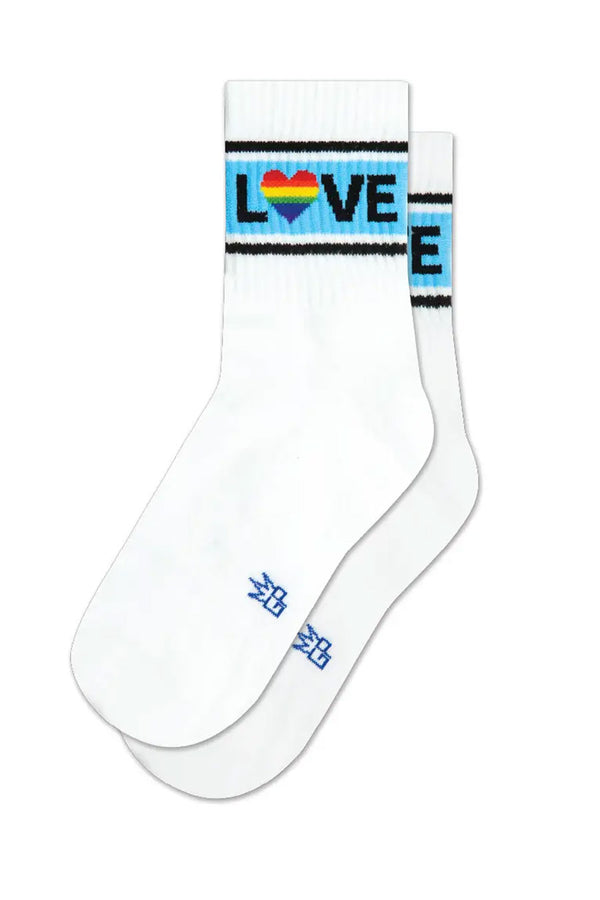White ankle crew socks. The socks have a blue stripe with two thin black stripes above and below it. Across the blue stripes in black lettering the socks say LOVE. The O is a heart shape with rainbow colors. White background. 