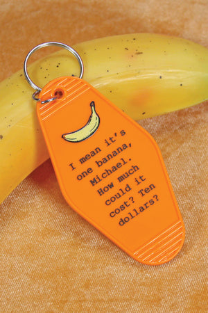 Orange plastic motel keychain that reads "I mean it's one banana, Michael. How much could it cost? Ten dollars?" A drawing of a yellow banana is above the quote from Arrested Development. Keychain is laying on a banana with a silver ring attached to the top. 