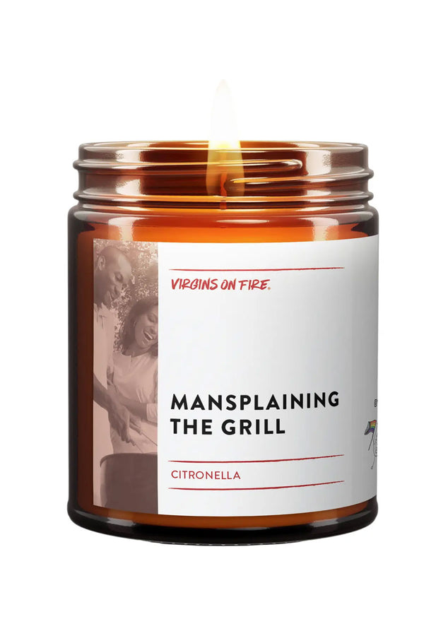 Amber glass candle jar with a white label. The label says Mansplaining the Grill with a black and white photo of a man holding tongs over a grill with a woman standing beside him. Scent is Citronella. White background.