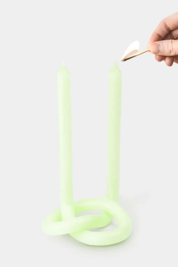 Someone lighting a twisted and knotted candle with two wicks at the end against a white background.