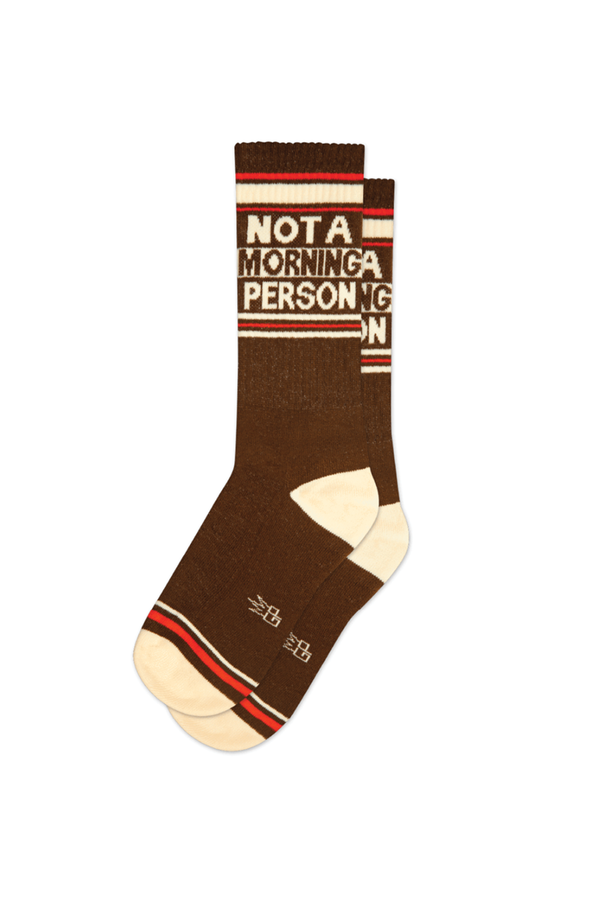 Brown Socks on a white background. The heel and toe are an ivory color. The top and around the toe is a red and ivory stripes. The socks read Not a Morning Person with ivory and red stripes underneath. 