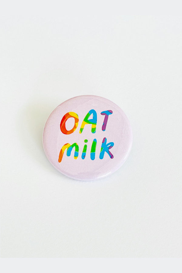 Lilac button on a white back ground. The button says Oat Milk with wavy rainbow colors. 